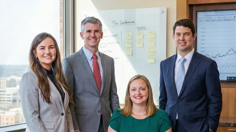 Office meeting with four people, two men and two women, smiling at a table with laptops.