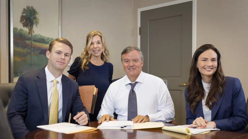 Group of four people in a meeting room, smiling at a table with documents.