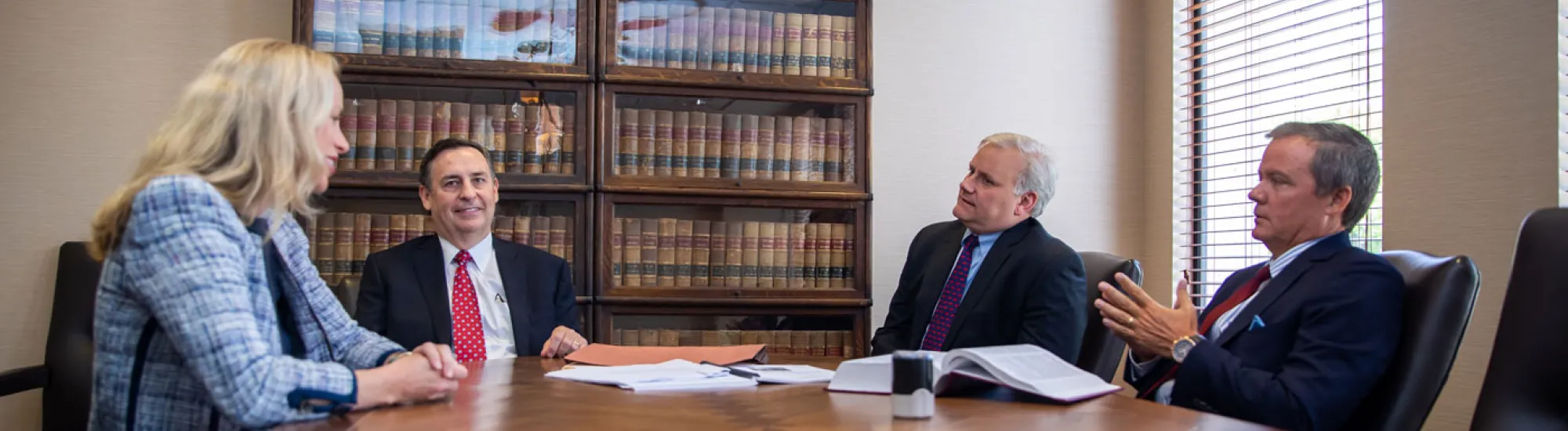 Four people in a conference room, discussing around a wooden table.